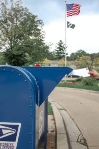 Crop person putting envelope in mailbox on street
