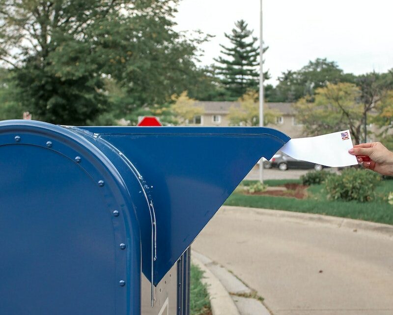 Crop person putting envelope in mailbox on street